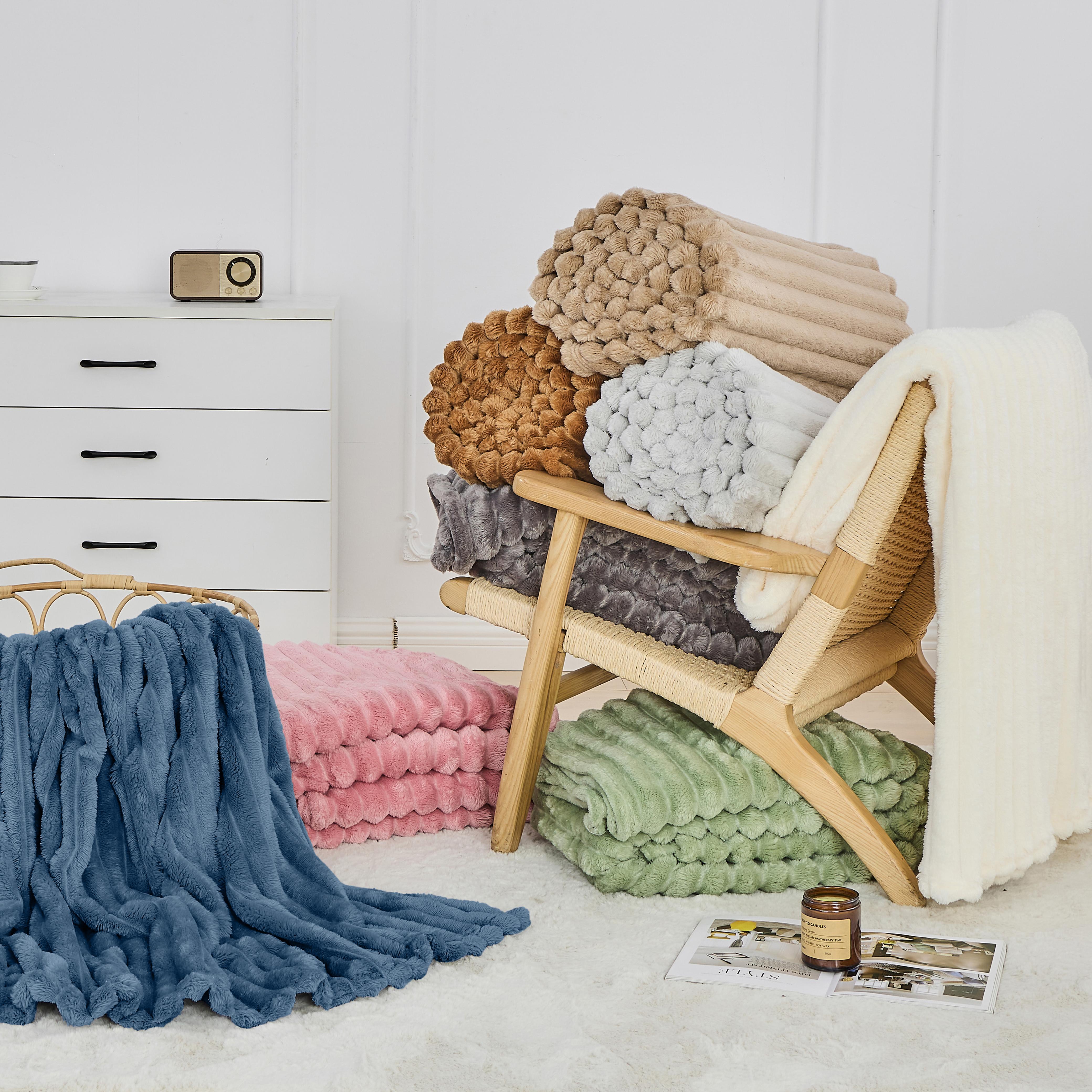 Stacks of colorful textured blankets on a wooden chair against a white wall.