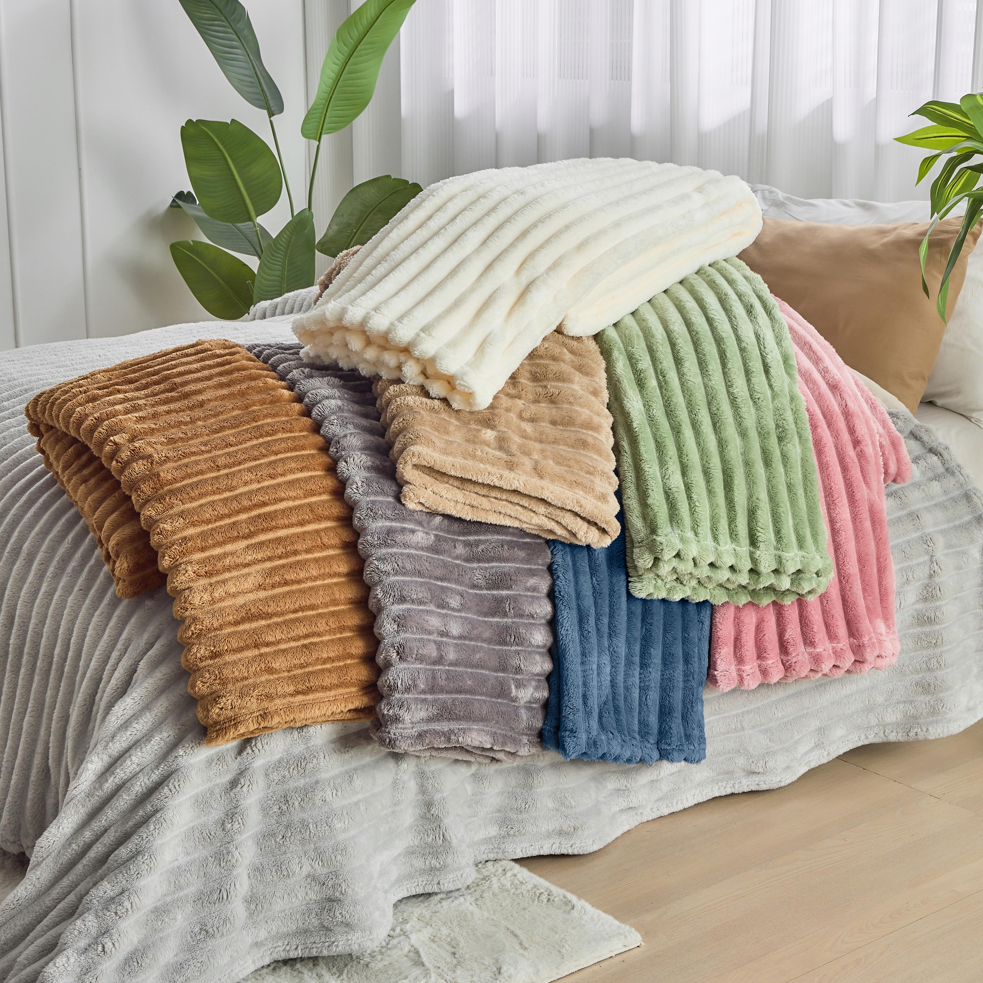 Stack of colorful textured blankets on a bed with plants in the background
