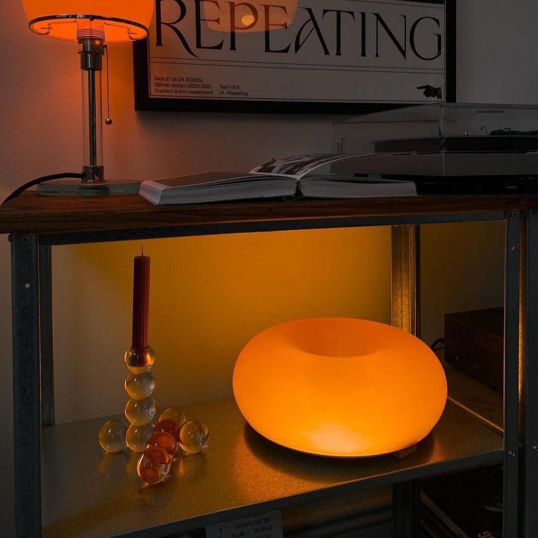 Orange lamp on a shelf with a framed picture and candle in the background