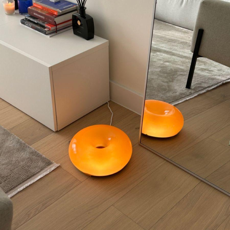 Orange floor lamp on a wooden floor with a mirror reflecting the room.