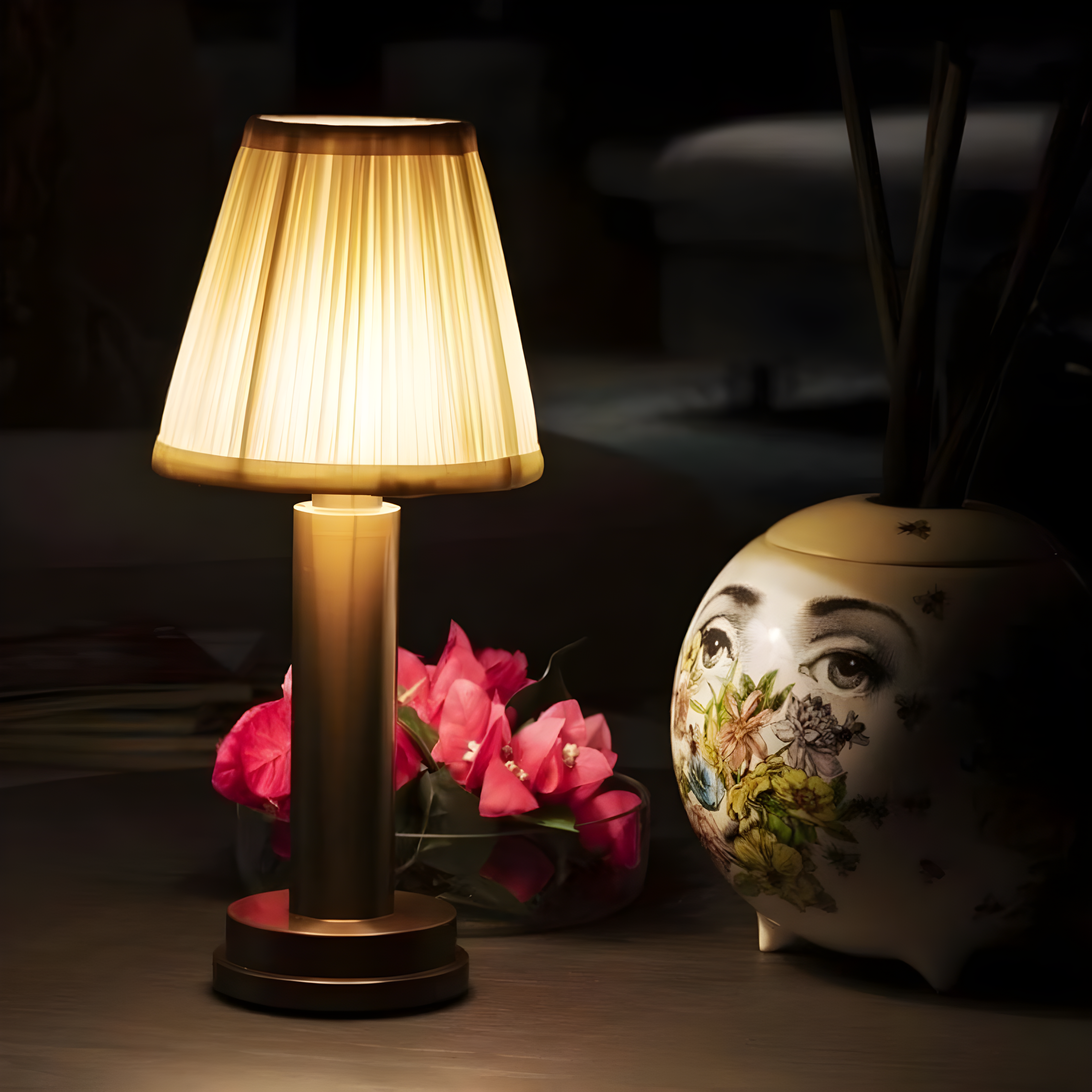 Table lamp with pleated shade, pink flowers, and decorative vase on a dark surface