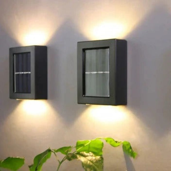 Two solar wall lights on a gray wall with a plant in the foreground.