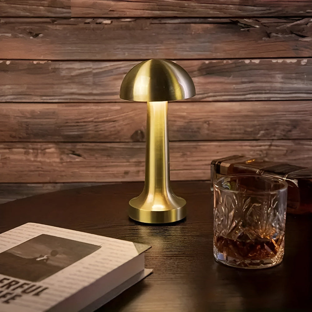 Gold mushroom lamp on a wooden table with a glass of whiskey and a book.