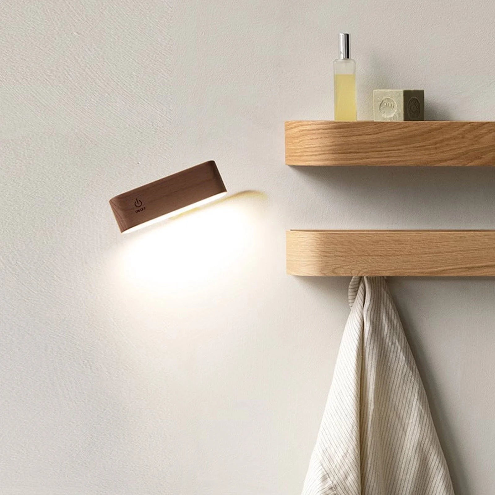 Wooden wall lamp and shelves with a towel and toiletries on a light gray wall.