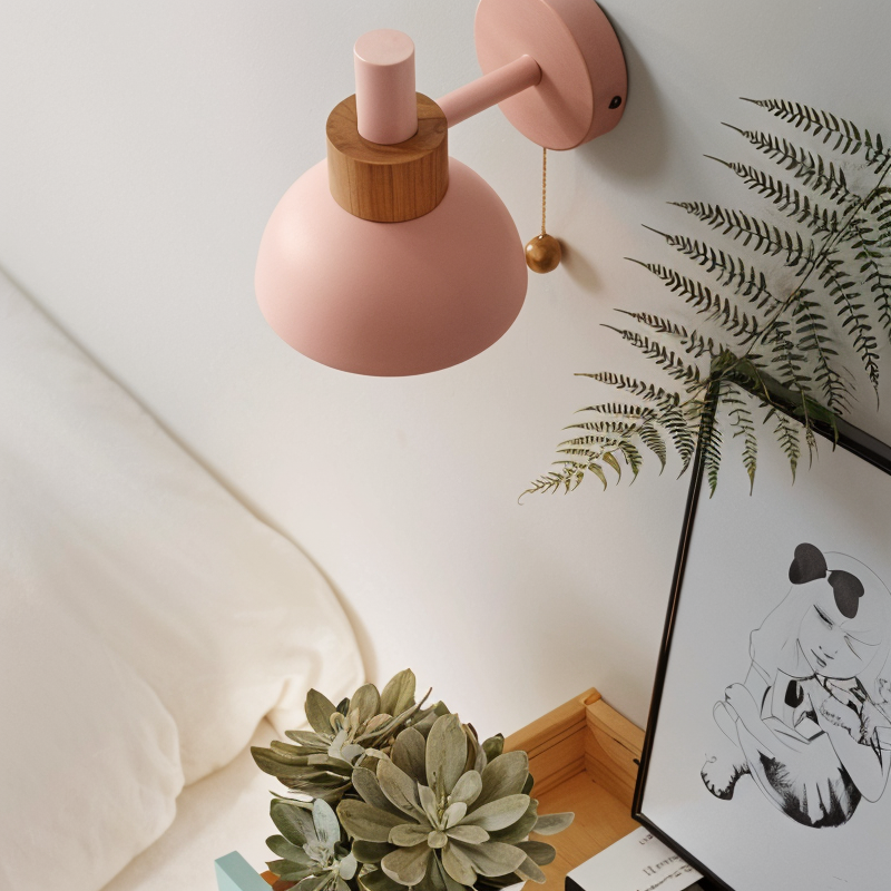 Pink wall lamp with wooden accent on a white wall, next to a plant and framed artwork.