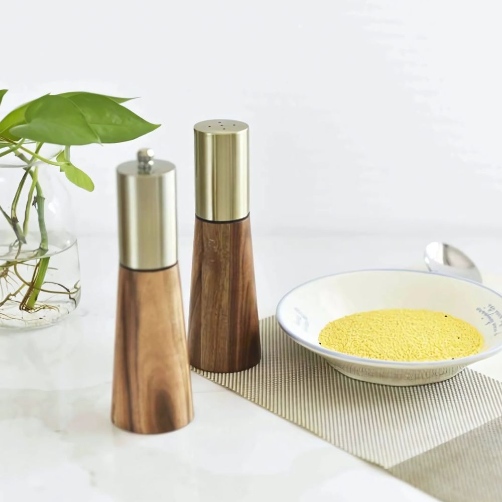 Wooden salt and pepper shakers on a table with a bowl of yellow powder and a plant.