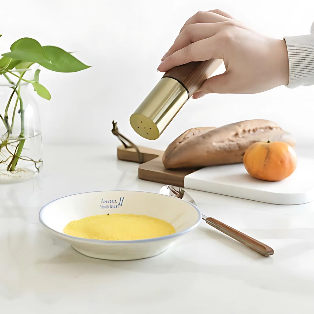 Hand using a pepper grinder over a bowl of food on a kitchen counter.