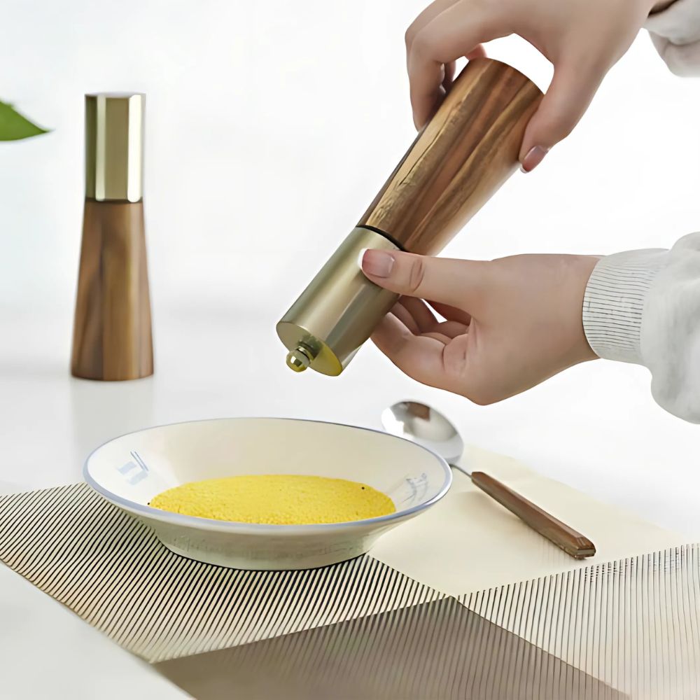 Hand using a pepper grinder on a plate with yellow food, with another pepper grinder in the background.