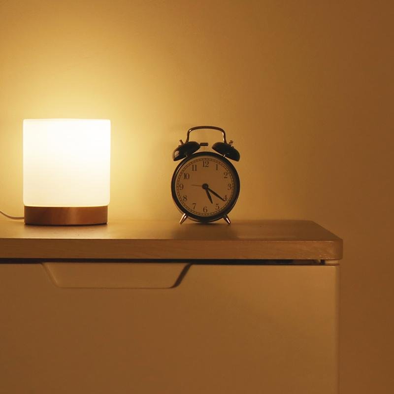 Small lamp and alarm clock on a wooden surface with a warm glow.