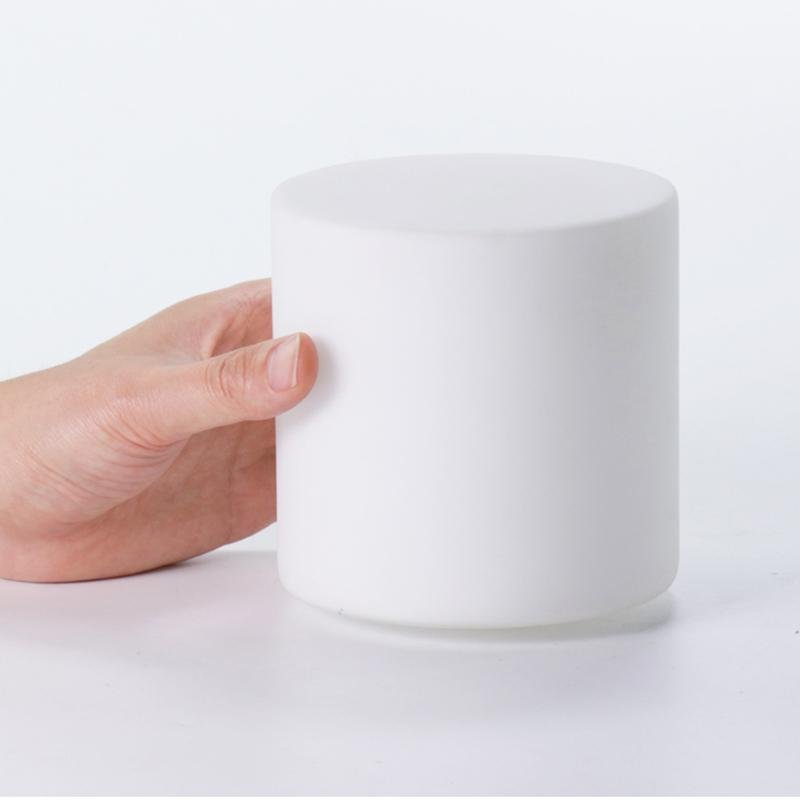 White cylindrical container held by a hand on a light gray background