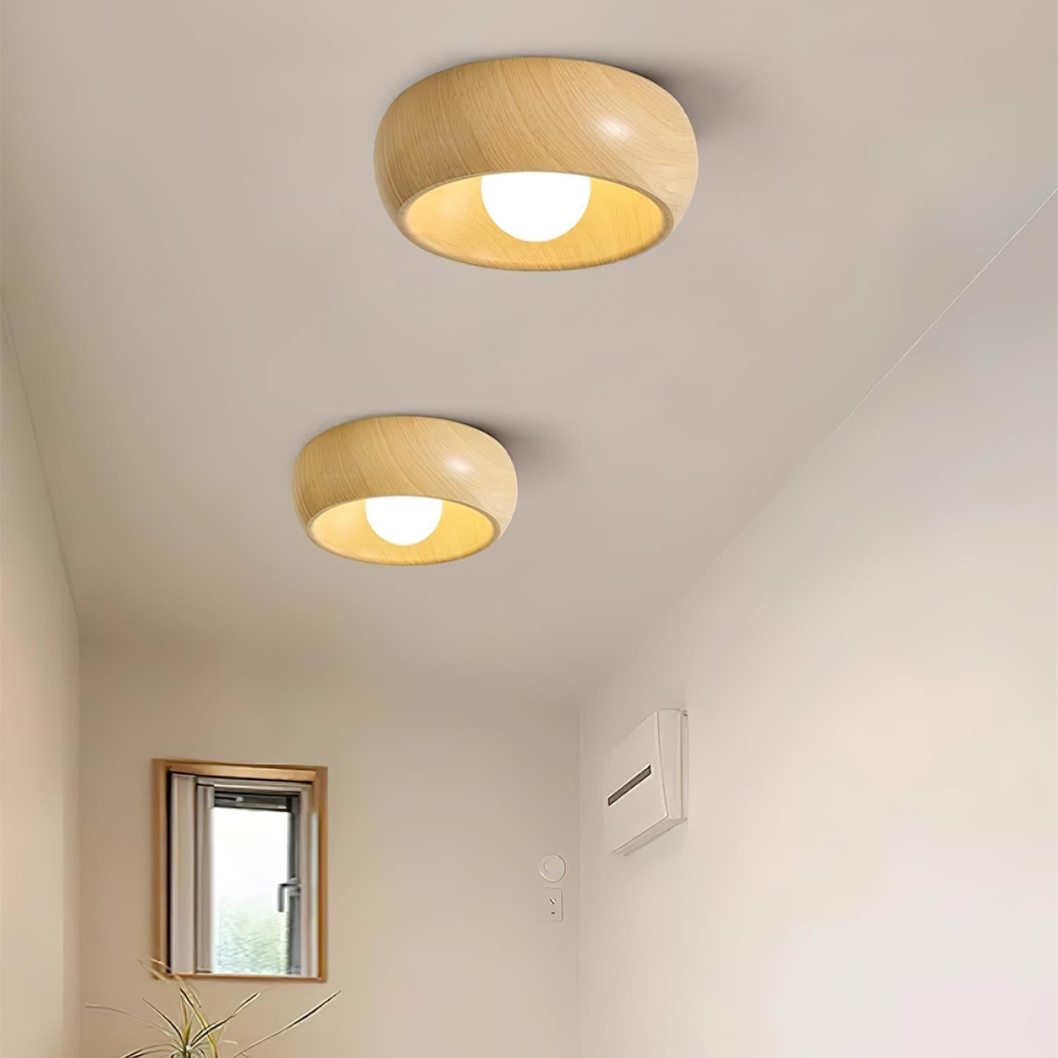 Two wooden ceiling lights on a white ceiling with a small window and plant in the background.