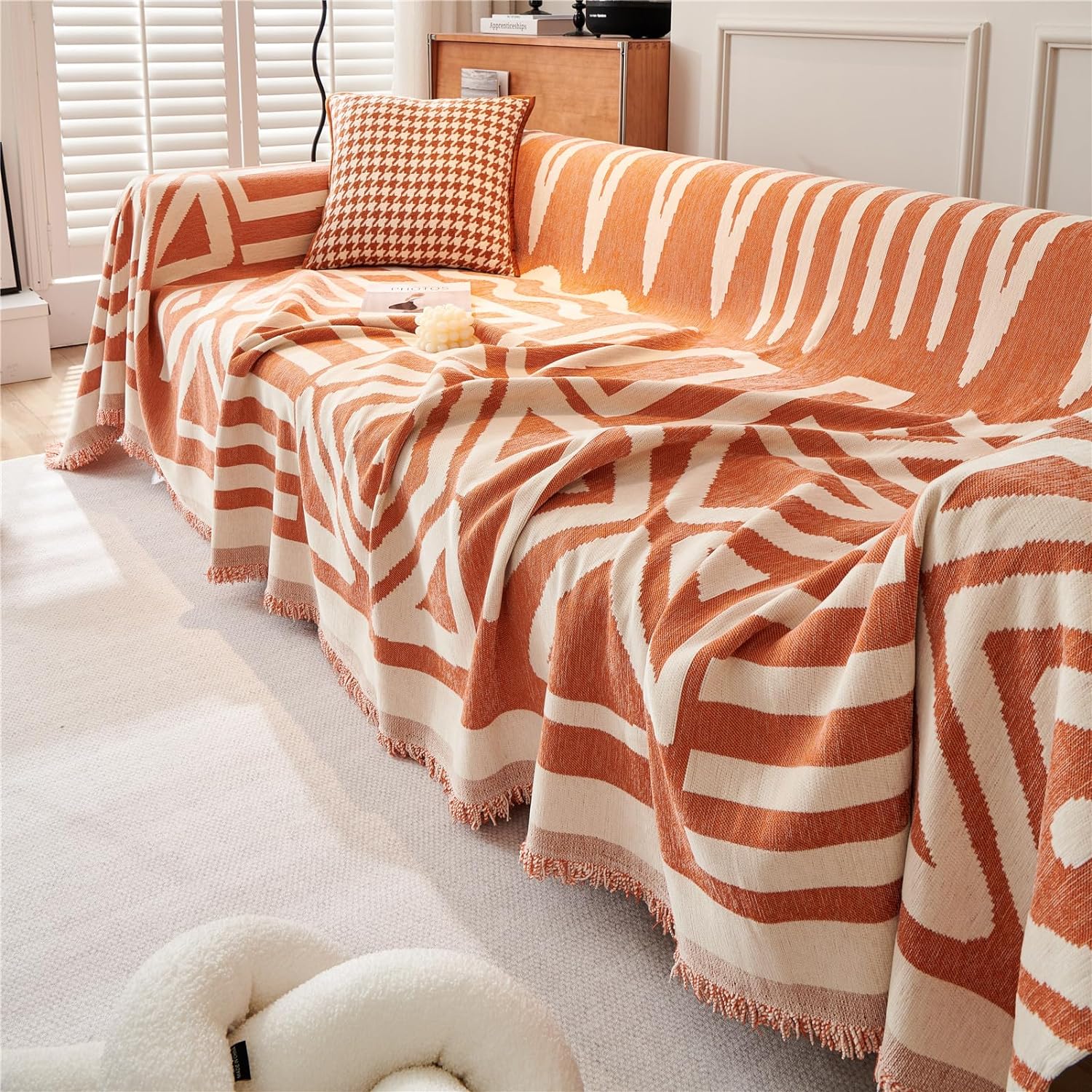 Orange and white patterned throw blanket draped over a sofa in a living room.