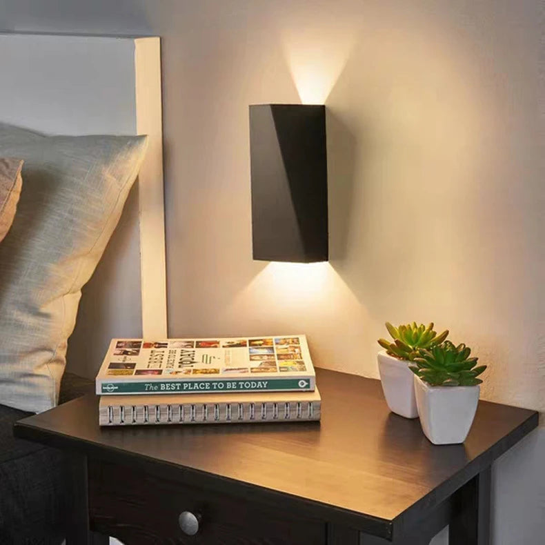 Book titled 'The Best Place to Be Today' on a nightstand with a wall lamp and plants.