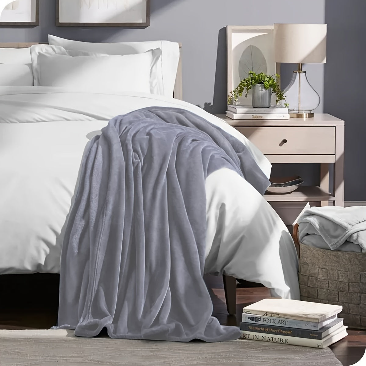 Gray blanket draped over a bed in a bedroom setting with a nightstand and books.