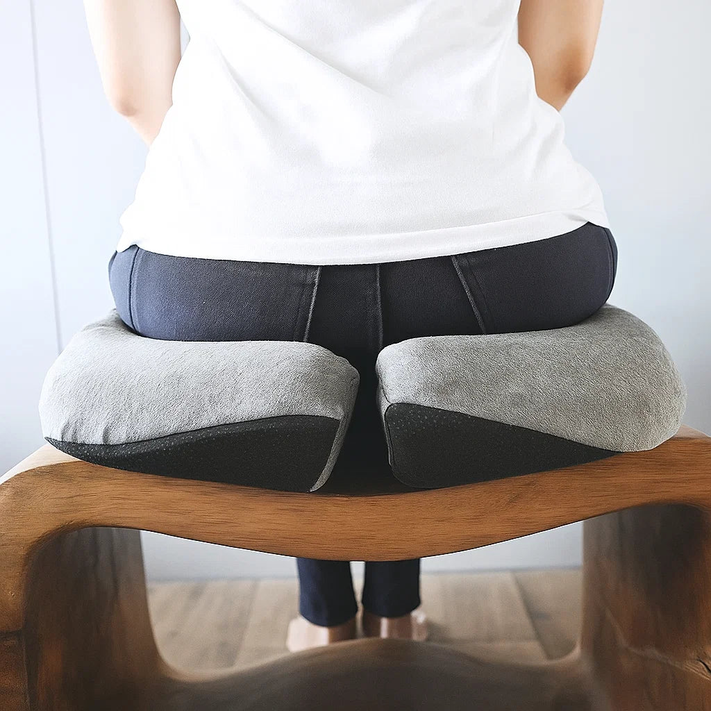 Person using a gray seat cushion on a wooden stool against a white background