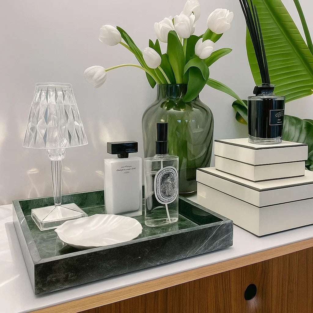 Decorative setup with a marble tray, lamp, books, and flowers on a surface.