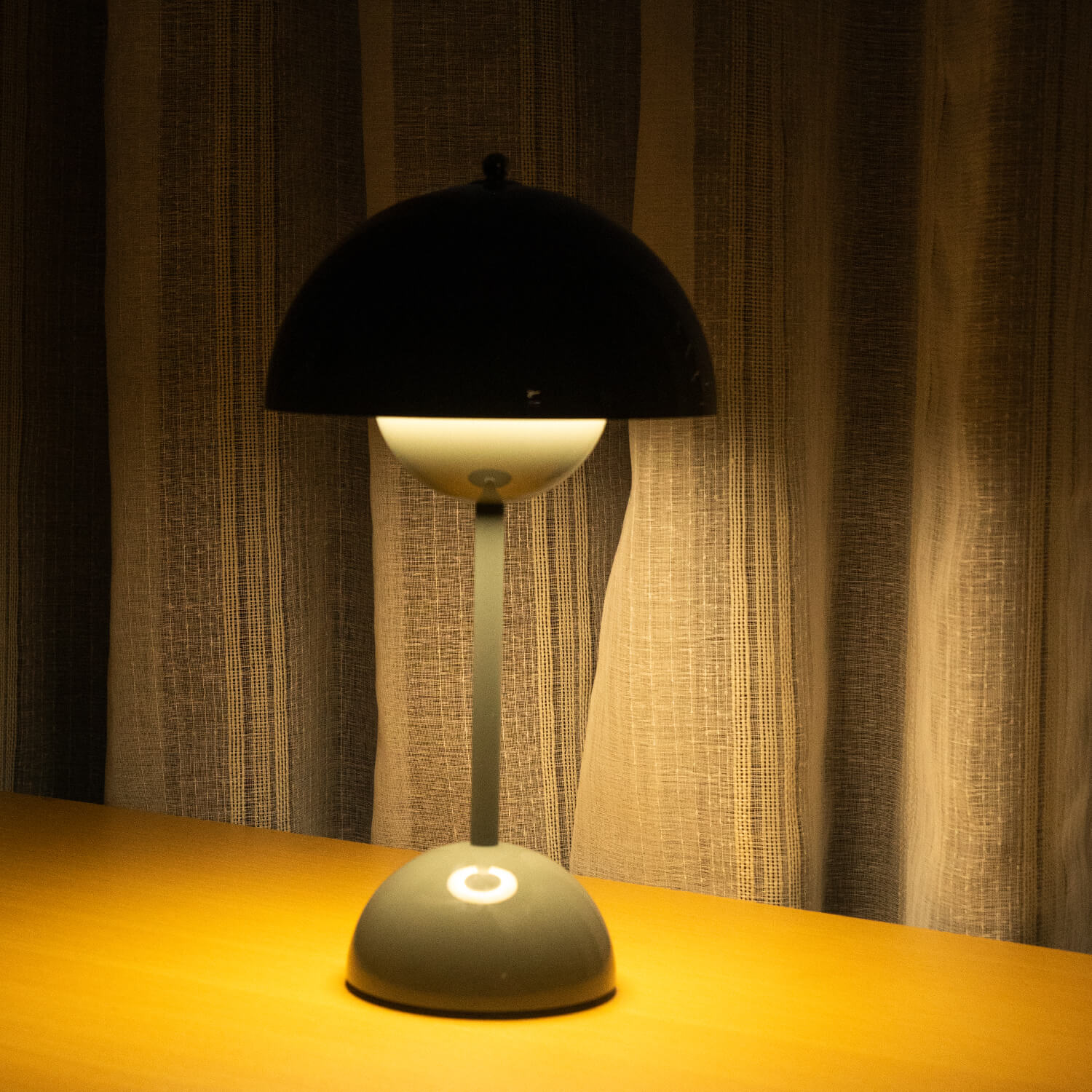 Table lamp with black shade and white base on a wooden surface with striped curtains in the background