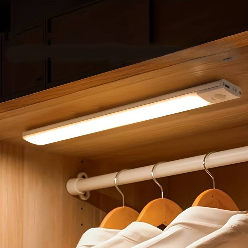 Under-cabinet light fixture in a wooden cabinet with clothes hanging on hooks.