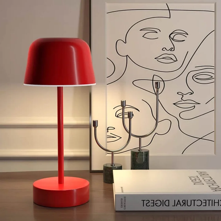 Red table lamp on a wooden surface with a minimalistic artwork in the background