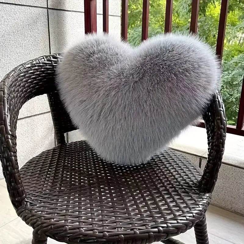Heart-shaped gray fur pillow on a wicker chair outdoors.