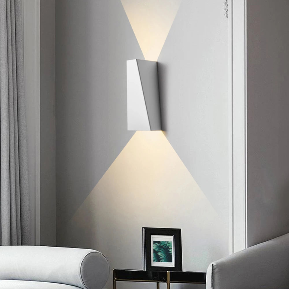 Modern wall-mounted lamp casting light on a gray wall with a gray sofa and framed picture in the foreground.