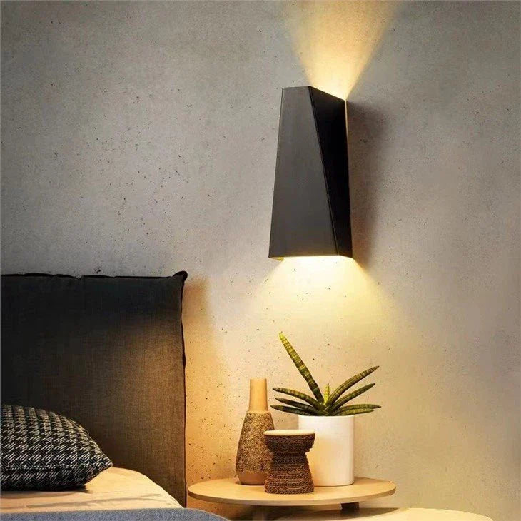 Modern wall-mounted light fixture on a textured wall above a bedside table with decorative items.