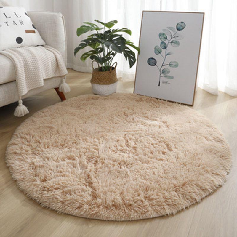 Round beige rug in a living room with a couch, plant, and wall art.