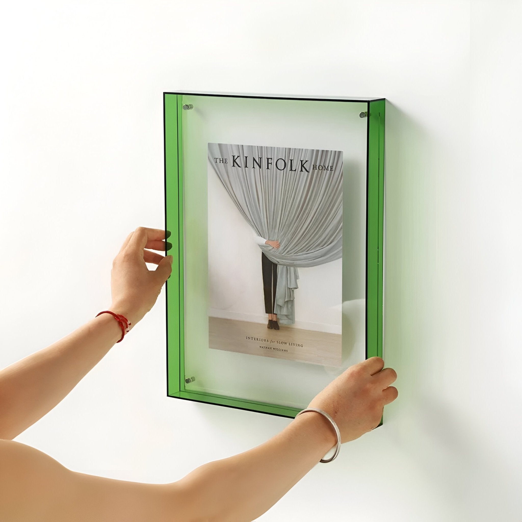 Person holding a green frame with a magazine cover inside against a white wall