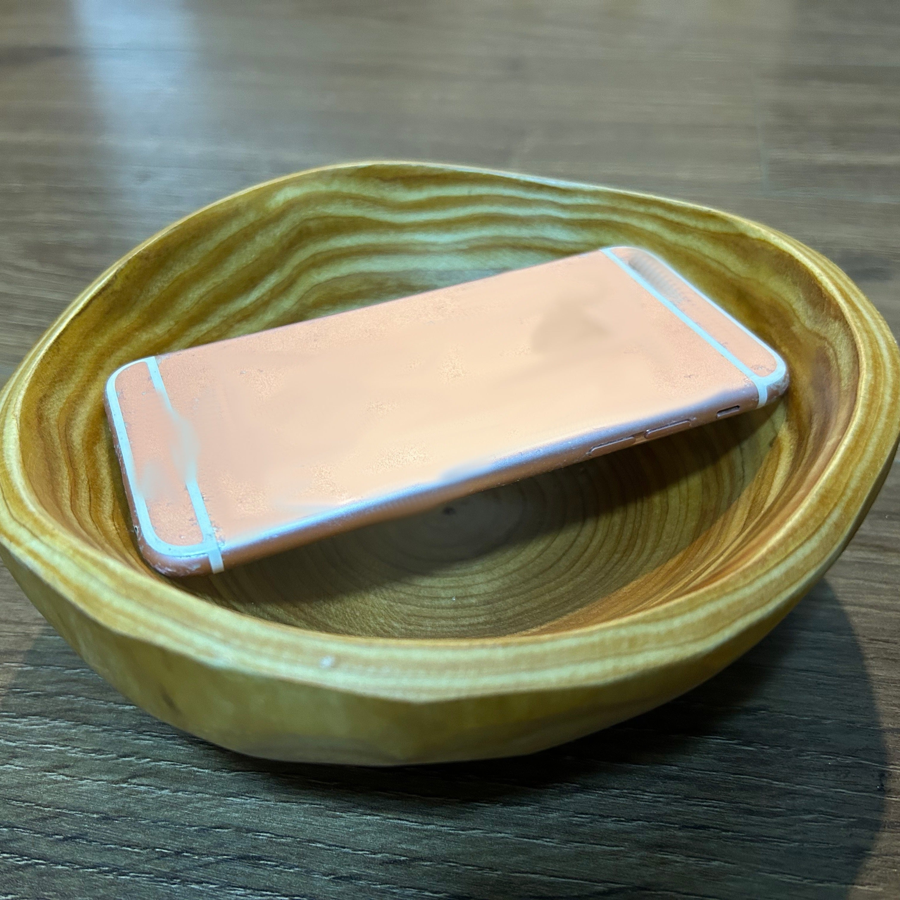 Phone with a pink case on a wooden bowl on a wooden surface