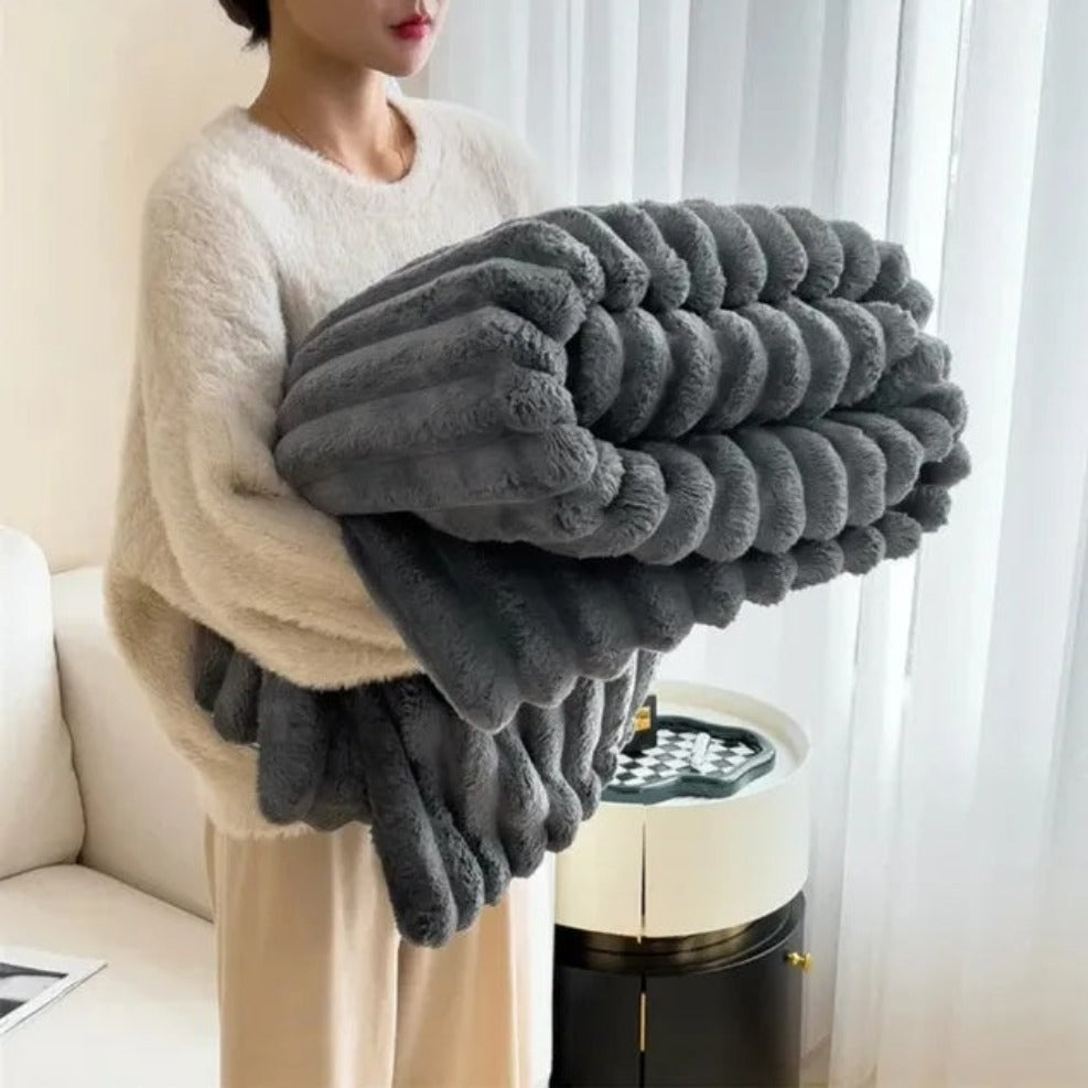 Person holding a large gray blanket in a room with a couch and window.