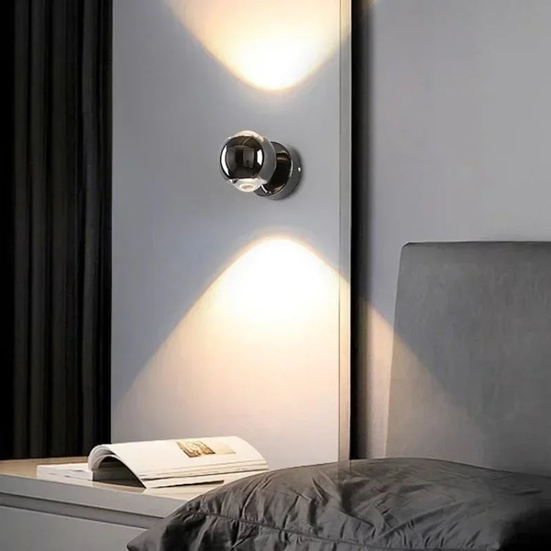 Modern wall light fixture on a gray wall with a bed and magazine in the foreground.