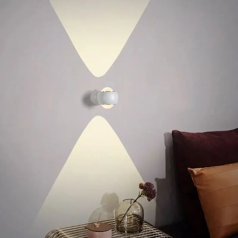 Modern wall light fixture casting geometric shadows on a wall with pillows and a vase in the foreground.