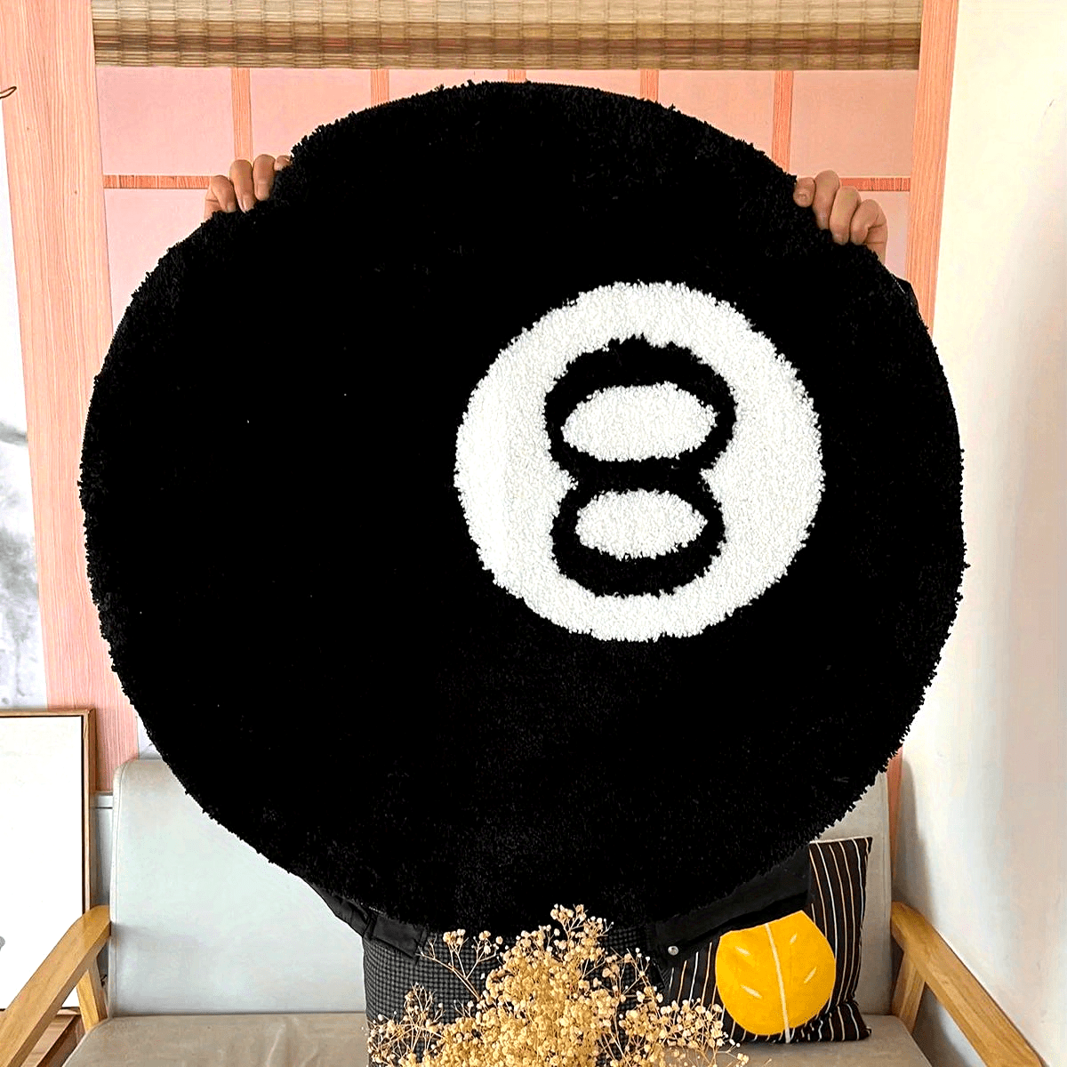 Round black rug with a white number 8 design held by two people in front of a wooden chair.