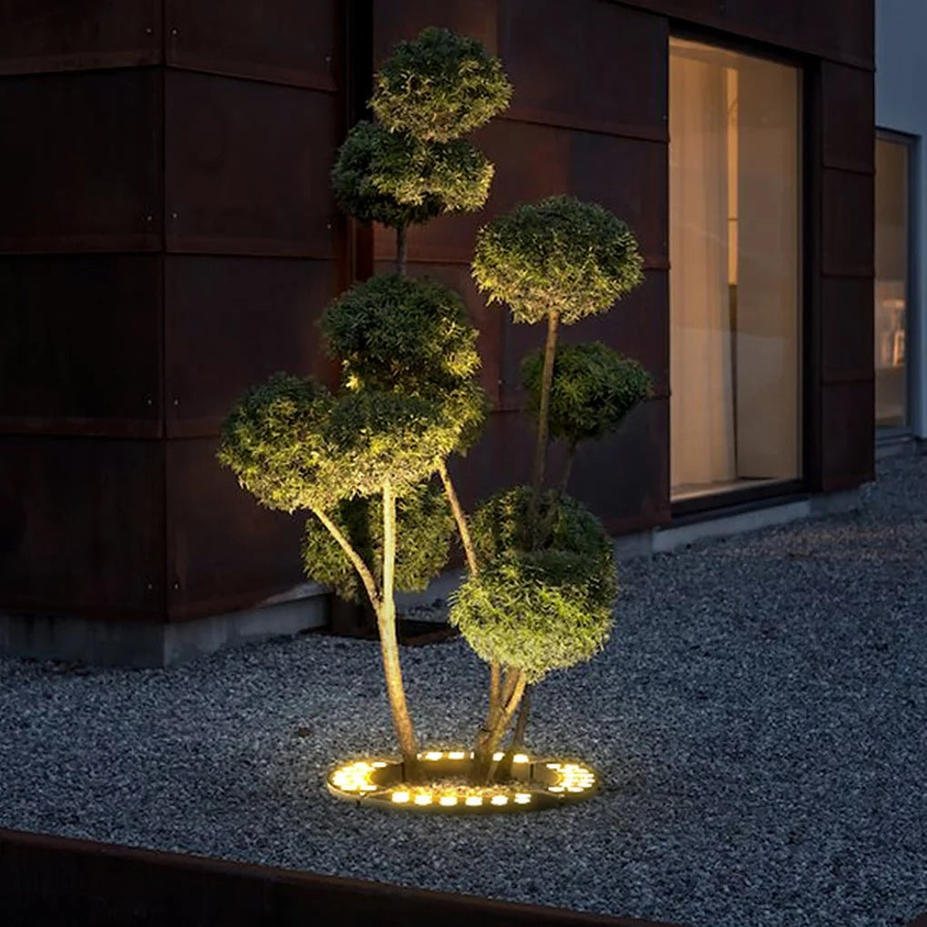 Decorative outdoor light fixture shaped like a tree on a gravel surface at night.