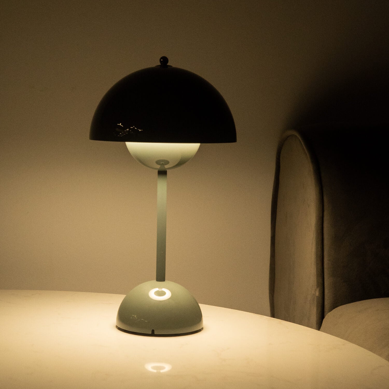Table lamp with black shade and green base on a table against a dark background