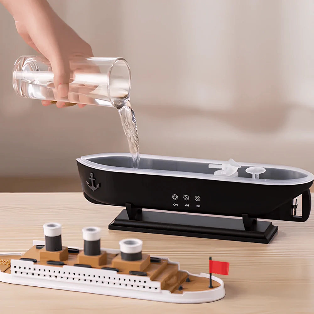 Hand pouring water into a black humidifier with a model ship on a wooden surface.