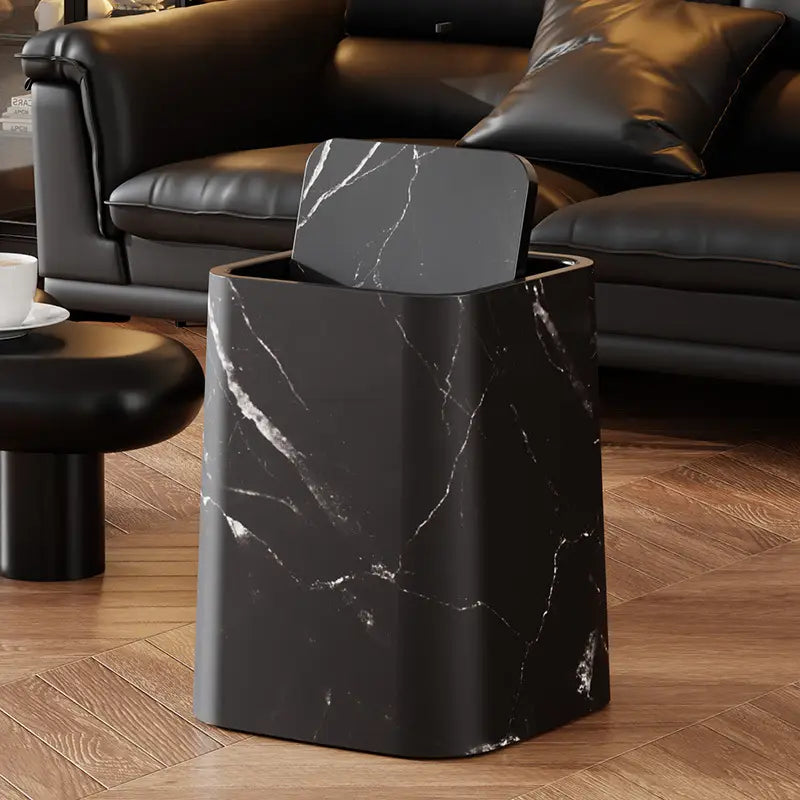Black marble-patterned trash can on a wooden floor with a dark leather sofa in the background.