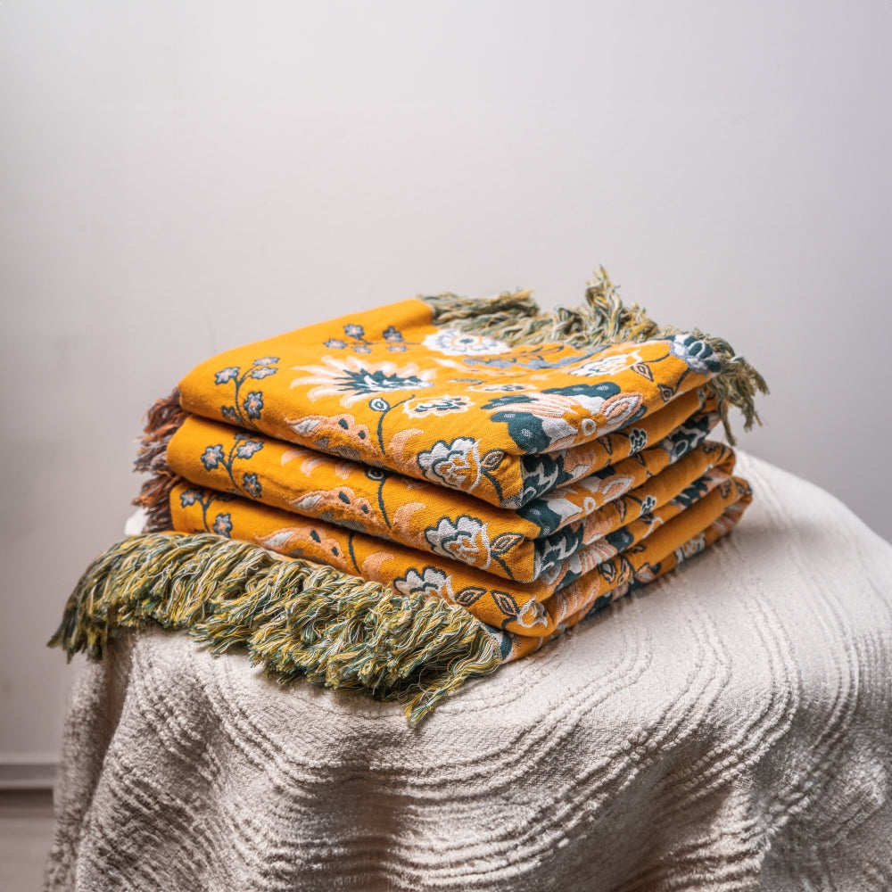 Stack of colorful patterned blankets with fringes on a textured surface.