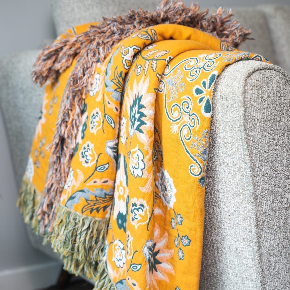 Yellow floral blanket with tassels draped over a gray couch.
