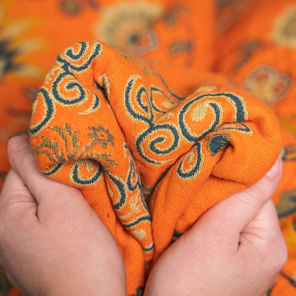 Orange fabric with intricate patterns held by hands against a matching fabric background