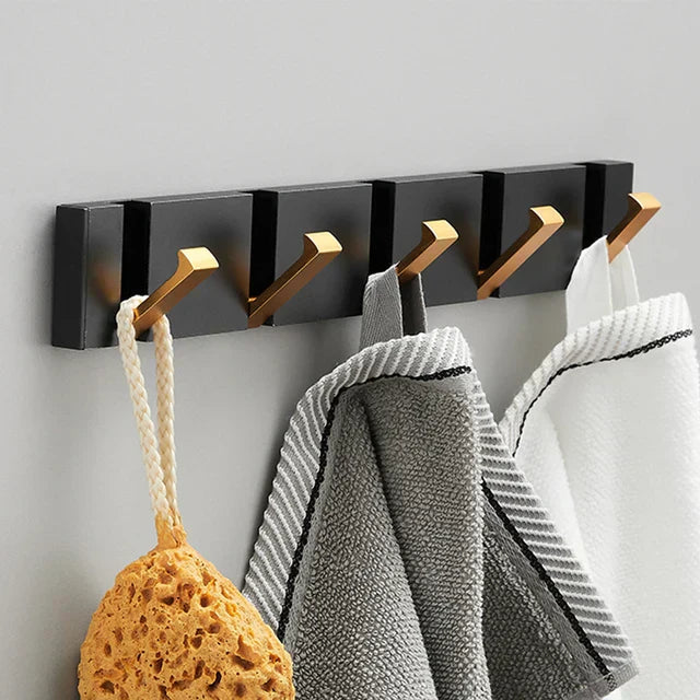 Wall-mounted coat rack with gold hooks holding a sponge and towels on a gray wall.