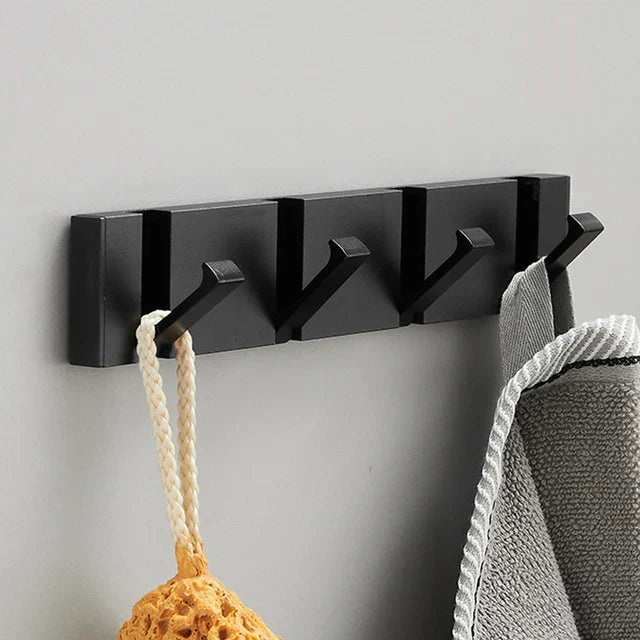 Black wall-mounted hook with multiple hooks holding a towel and a scrubber against a gray background