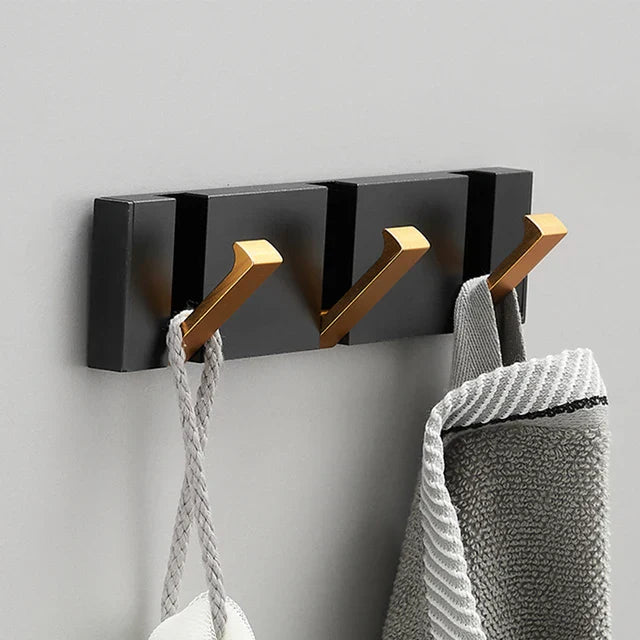 Black wall hook with gold hooks holding towels on a gray background