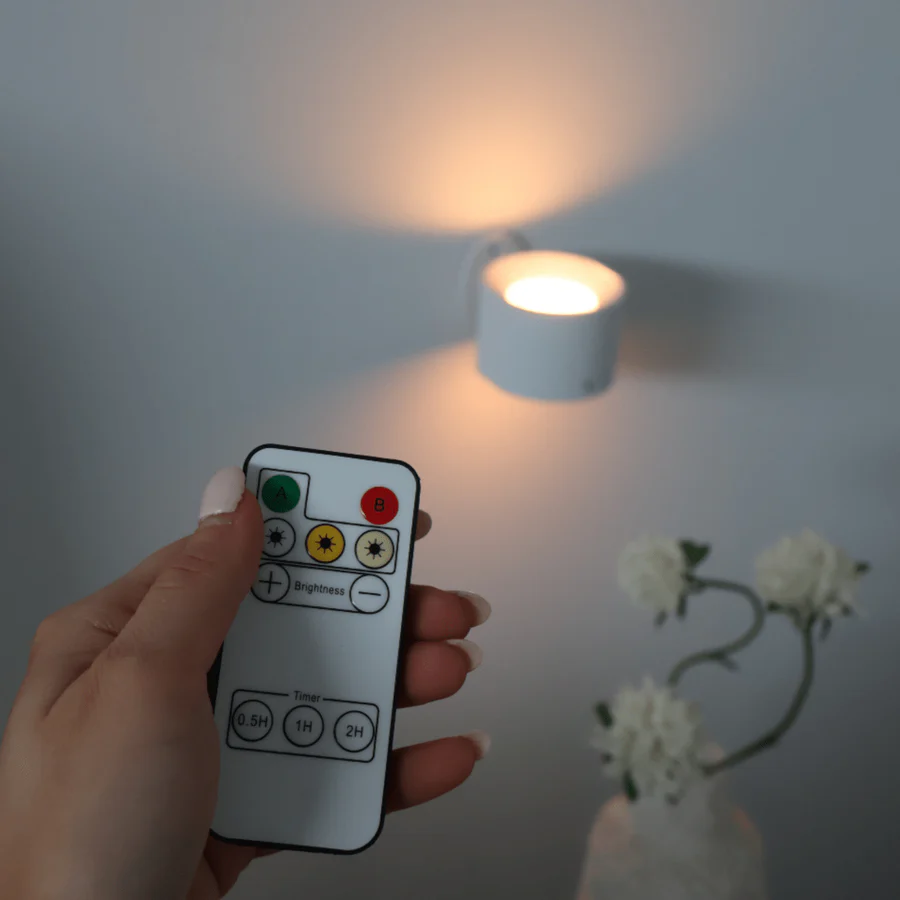 Hand holding a remote control near a small light bulb on a plain background