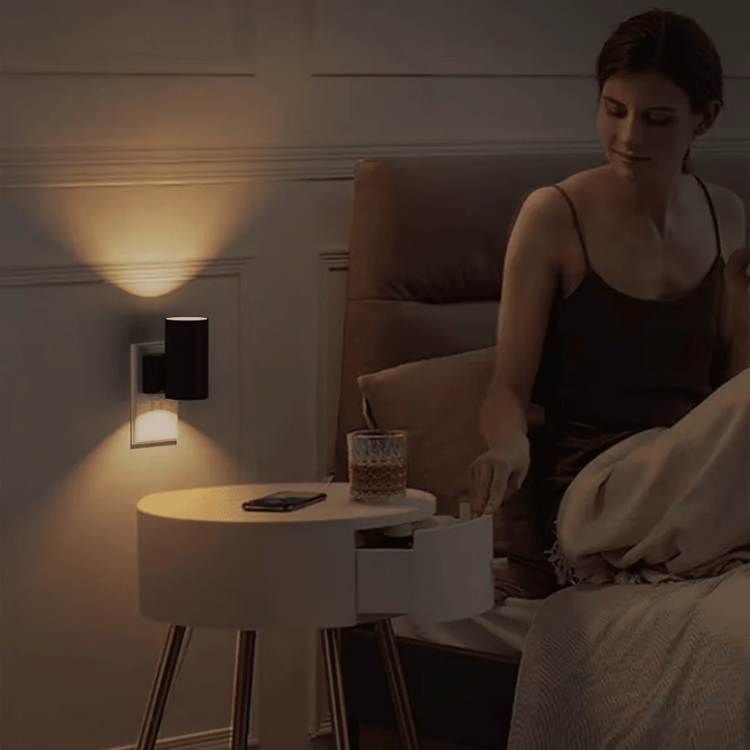 Woman sitting on a bed next to a nightstand with a lamp and phone.
