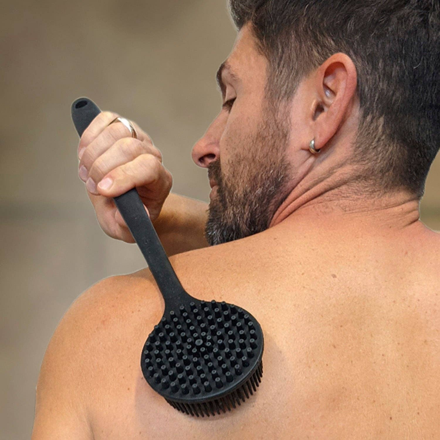 Man using a black brush on his back with a blurred background