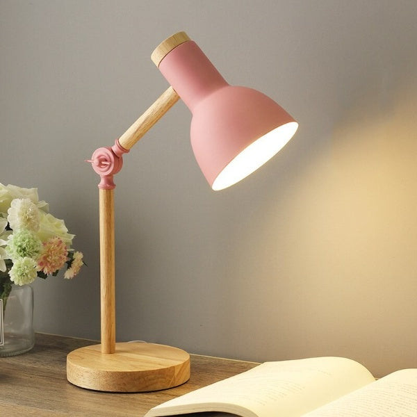 Pink and wooden desk lamp on a table with a book and flowers in the background