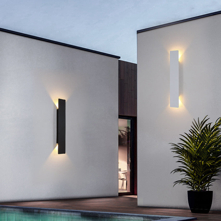 Modern outdoor wall lights on a building exterior with a pool and plant.