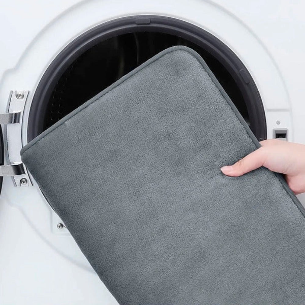 Person holding a gray mat over an open washing machine.