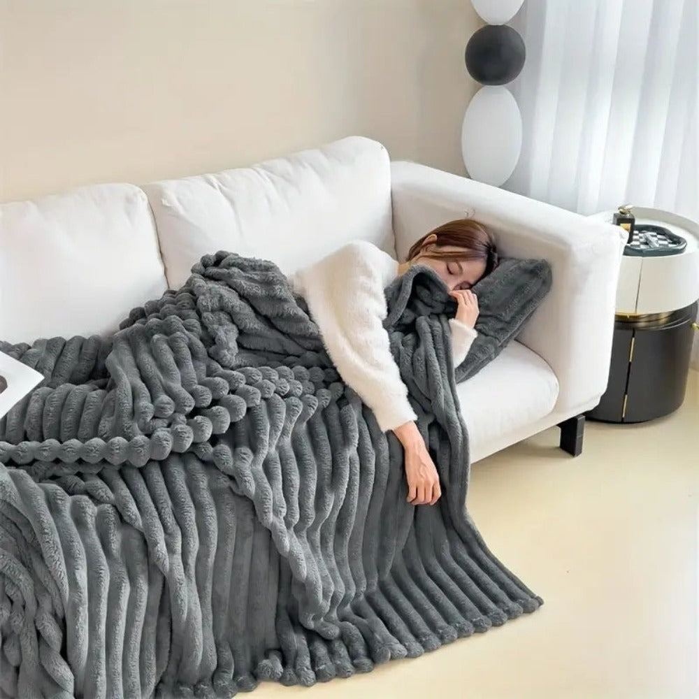 Person lying on a white couch under a gray textured blanket in a cozy living room.